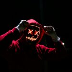pexels-photo-1097456-1097456 A spooky illuminated mask figure with a red hoodie in a dark setting, perfect for Halloween themes.